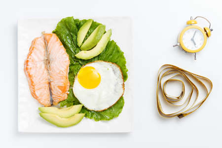 Plate with fish and vegetables, yellow alarm clock on white background.の写真素材