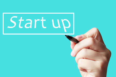 Female hand writes with marker start-up on blue background front view.の写真素材