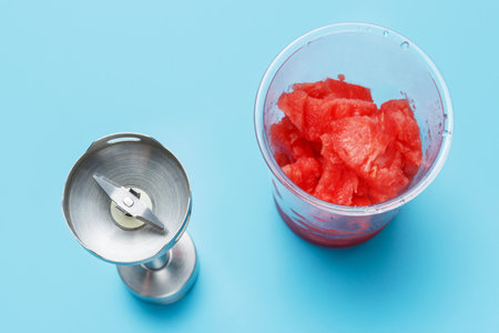 Hand blender and ladle with slices of watermelon on blue background top view.の写真素材