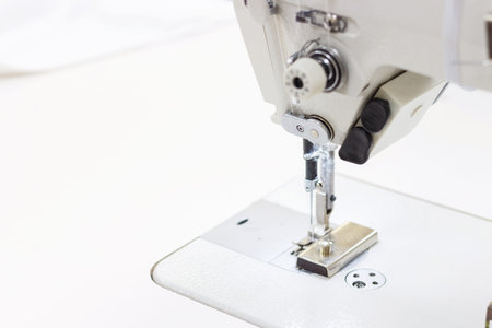 White sewing machine with blue threads close-up, side view.