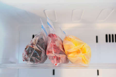 Frozen fruits in plastic bags in freezer close-up, front view.の写真素材