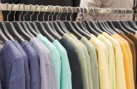 Multicolored woolen knitted sweaters hanging on hangers close-up.の写真素材