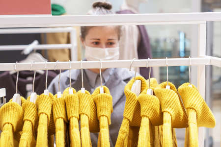 Young woman chooses yellow sweaters on hangers in store, selective focus.の写真素材