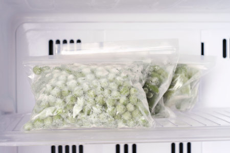 Frozen green pea in bags in freezer close-up, front view