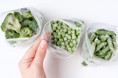 Female hand holding plastic bag with frozen green peas on a white background top view.の写真素材