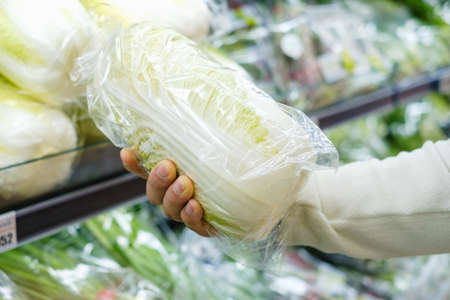 In the supermarket a male hand holds a Chinese cabbage close-up.の写真素材