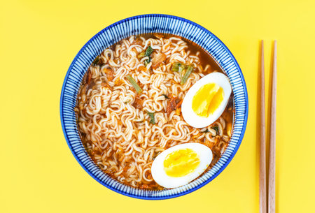 Ramen noodles with broth and eggs in a bowl close-up top view on yellow background.