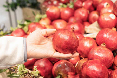 A man holding a pomegranate fruit in a supermarket close-up.の写真素材