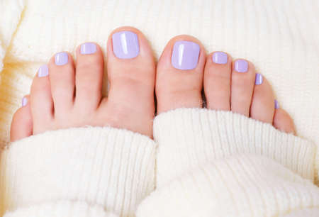 Female feet with purple pedicure on white knitted surface, top view.の写真素材