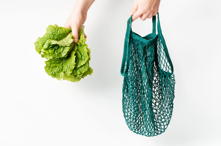 Female hands hold a green string bag and lettuce on white background close-up.の写真素材