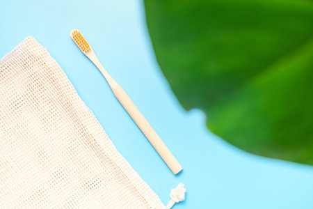 Bamboo toothbrush and green plants on blue background close-up, top view.