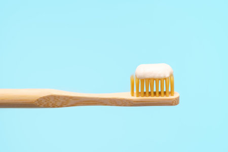 Bamboo toothbrush with toothpaste on blue background close-up.