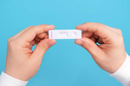 Male hands holding a homemade test for coronavirus close-up on a blue background.の写真素材