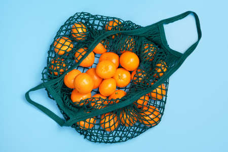 Mandarins in a green string bag close-up on blue background, top view.の写真素材