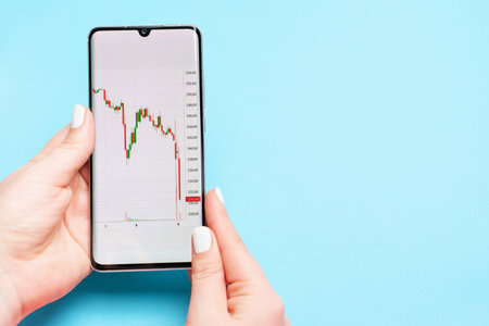 Female hand holding a phone with a stock market graph on blue background.