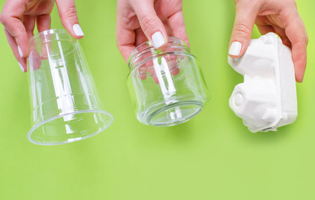 Female hands holding cardboard and glass jar on green background, garbage sorting concept.