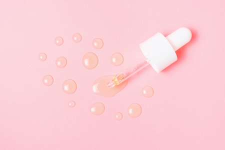 Glass pipette and drops of serum on a pink background close-up.