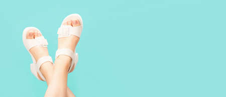 Female legs with white pedicure in summer sandals on blue background, copy space.の写真素材