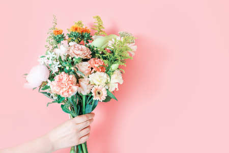 Female hands holding a bouquet of pink flowers close-up on a pink background, copy space.の写真素材