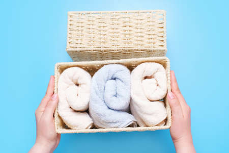 Female hands hold wicker box with rolled towels inside on a blue background top view.の写真素材