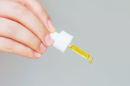 Female hand holds a dropper with serum close-up on gray background.