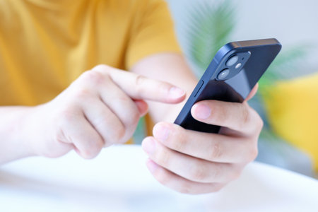 Seoul, South Korea - 25.05.2022: Man in yellow t-shirt holding iPhone 12 close-up, side view.のeditorial素材
