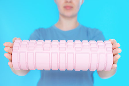 Young woman hold a massage foam roller on blue background close-up, selective focus.の写真素材