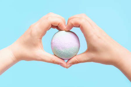 Female hands in the shape of a heart holding a bath bomb close-up on a blue background.の写真素材