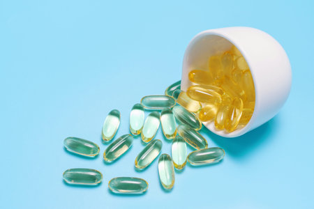 Scattered omega-3 capsules in a white glass close-up on a blue background.
