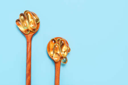 Fish oil capsules in wooden spoons close-up on a blue background copy space.の写真素材