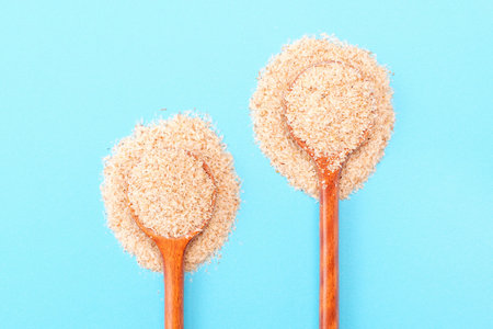 Two wooden spoons of psyllium husk on a blue background top view, close up.