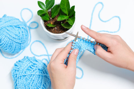Female hands are knitting from yarn on white background, top view .