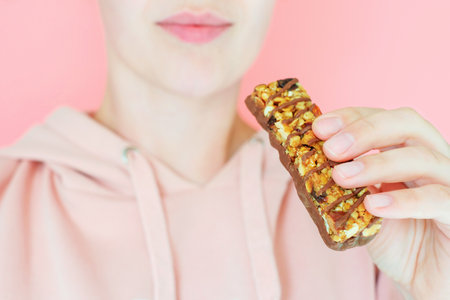 Young woman holding protein bar close-up on pink background, selective focus.の写真素材
