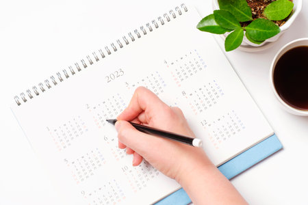 Female hands write in calendar 2023 on white background, concept of planning.