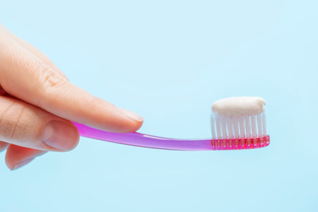 Hand holding pink toothbrush with toothpaste on a blue background close-up, side view.