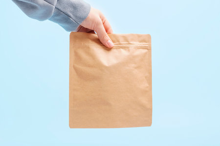 Female hand holding zip paper bags on blue background, copy space.の写真素材