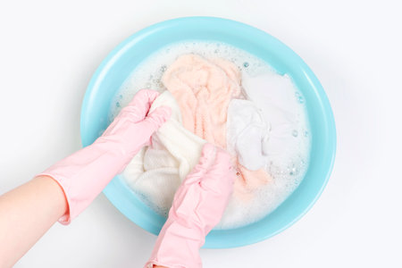 Female hands in pink gloves washes clothes with powder in a basin on a white background close-up top view.の写真素材
