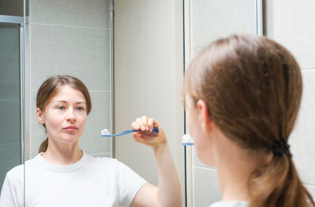 Young woman brushing teeth standing in front of mirror, oral care concept.の写真素材