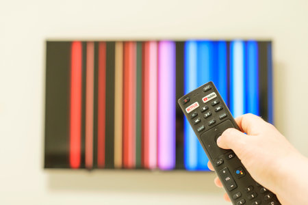 Seoul - 05.02.2023: hand holds the remote for netflix application on the background of the tv.のeditorial素材