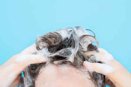 A girl washes her hair with shampoo on blue background, front view.の写真素材