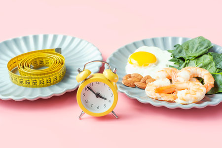 Plate with food and plate with measuring tape on pink background front view, intermittent fasting concept.の写真素材