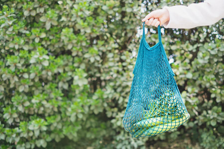 Hand holding reusable shopping bag with vegetables on green background, zero waste concept.の写真素材