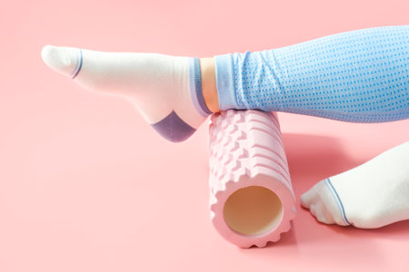 Female leg rolls a massage foam roller close-up on pink background, side view.の写真素材