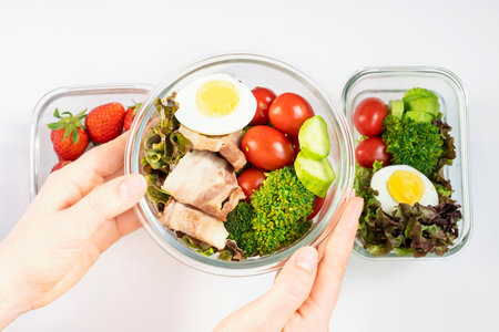 Female hand holding glass lunch box with healthy food top view.