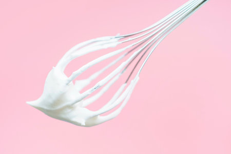 Whisk with whipped cream on pink background close-up.の写真素材