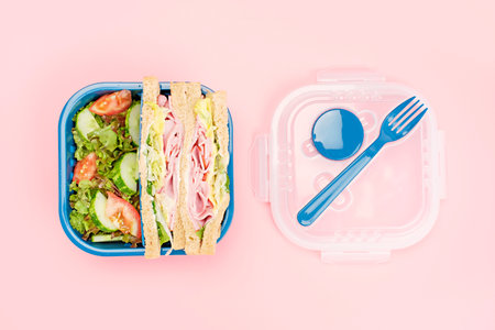 Plastic lunch box with sandwich and salad on pink background from above, food concept for office or school.の写真素材