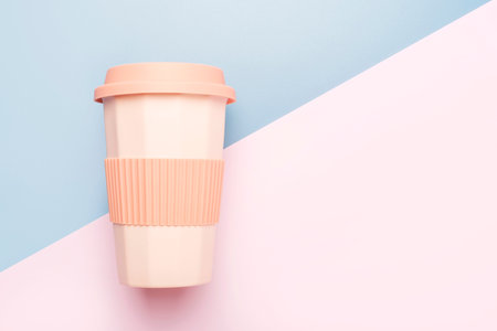Reusable ceramic glass for coffee with silicone lid on blue and pink background, top view.の写真素材