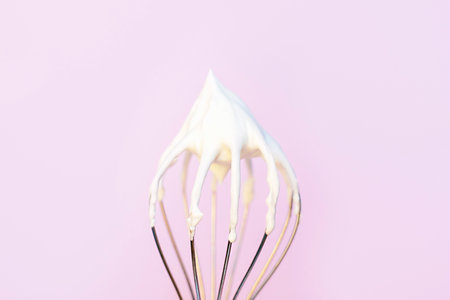 Whisk with whipped cream on light pink background close-up.の写真素材
