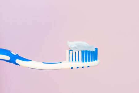Toothbrush with white toothpaste close-up on pink background.