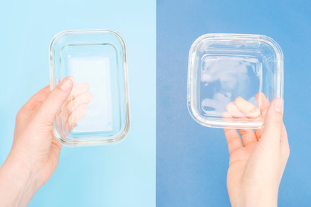 A female hand holds glass boxes for food on blue background, top view.の写真素材